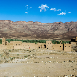 Picture of a desert village with earthen buildings set against a backdrop of rocky mountains