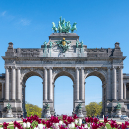 Picture of a large triumphal arch with statues on top, framed by colorful flowers in the foreground